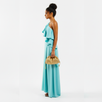 Woman wearing a turquoise dress holding a gold clutch against a white background