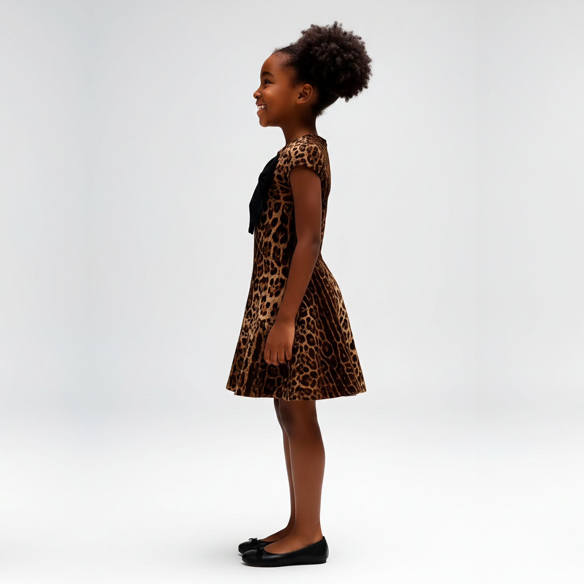 Child wearing a leopard print dress with a large black bow on a gray background