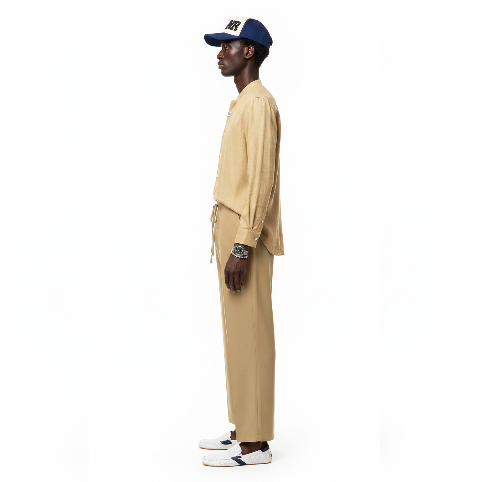 Man wearing a beige outfit with a navy cap on a white background