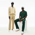 Two individuals wearing beige and green outfits with hats on a white background