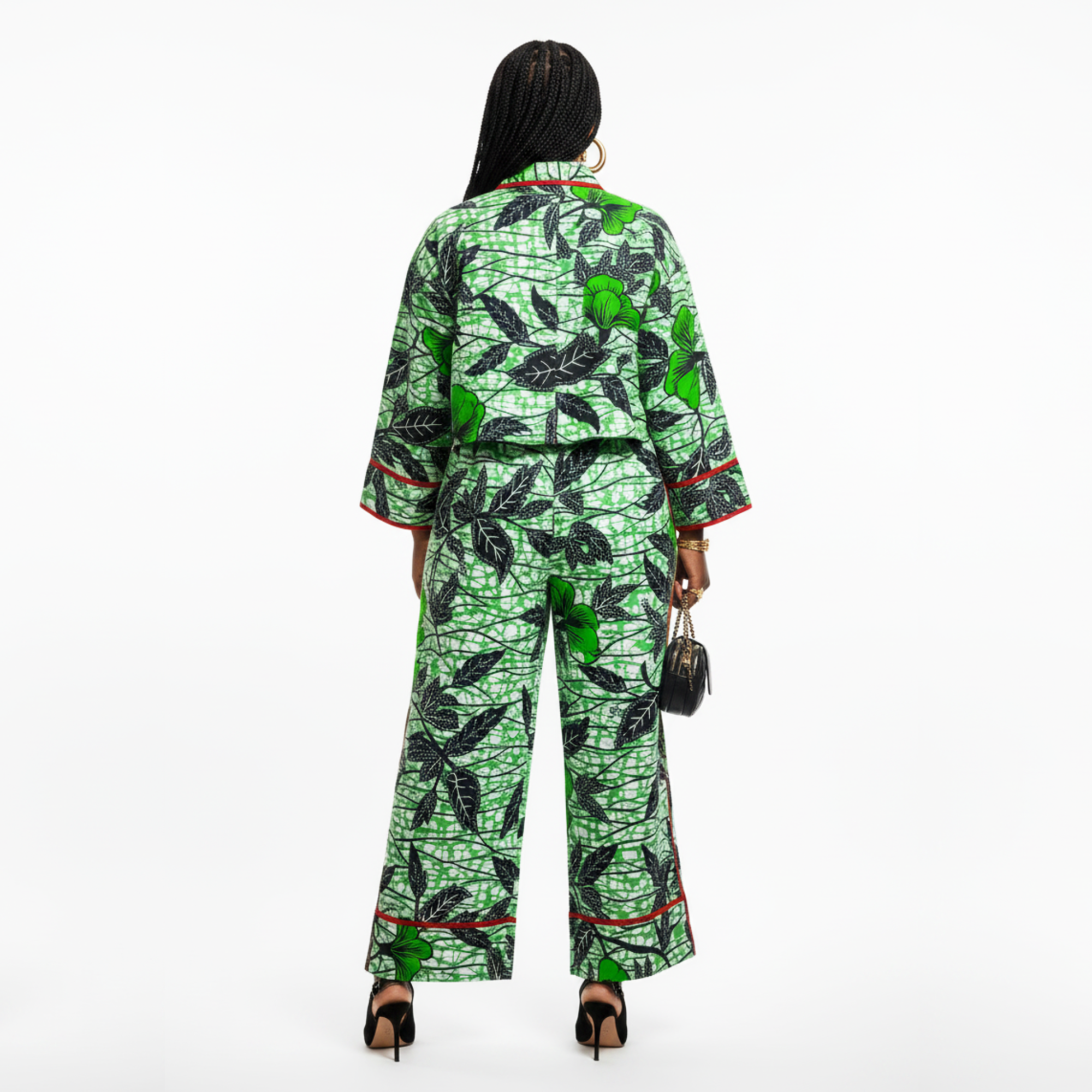 A woman shown from the back wearing a matching two-piece outfit with a green and black leaf pattern and red piping, photographed against a plain white studio background.