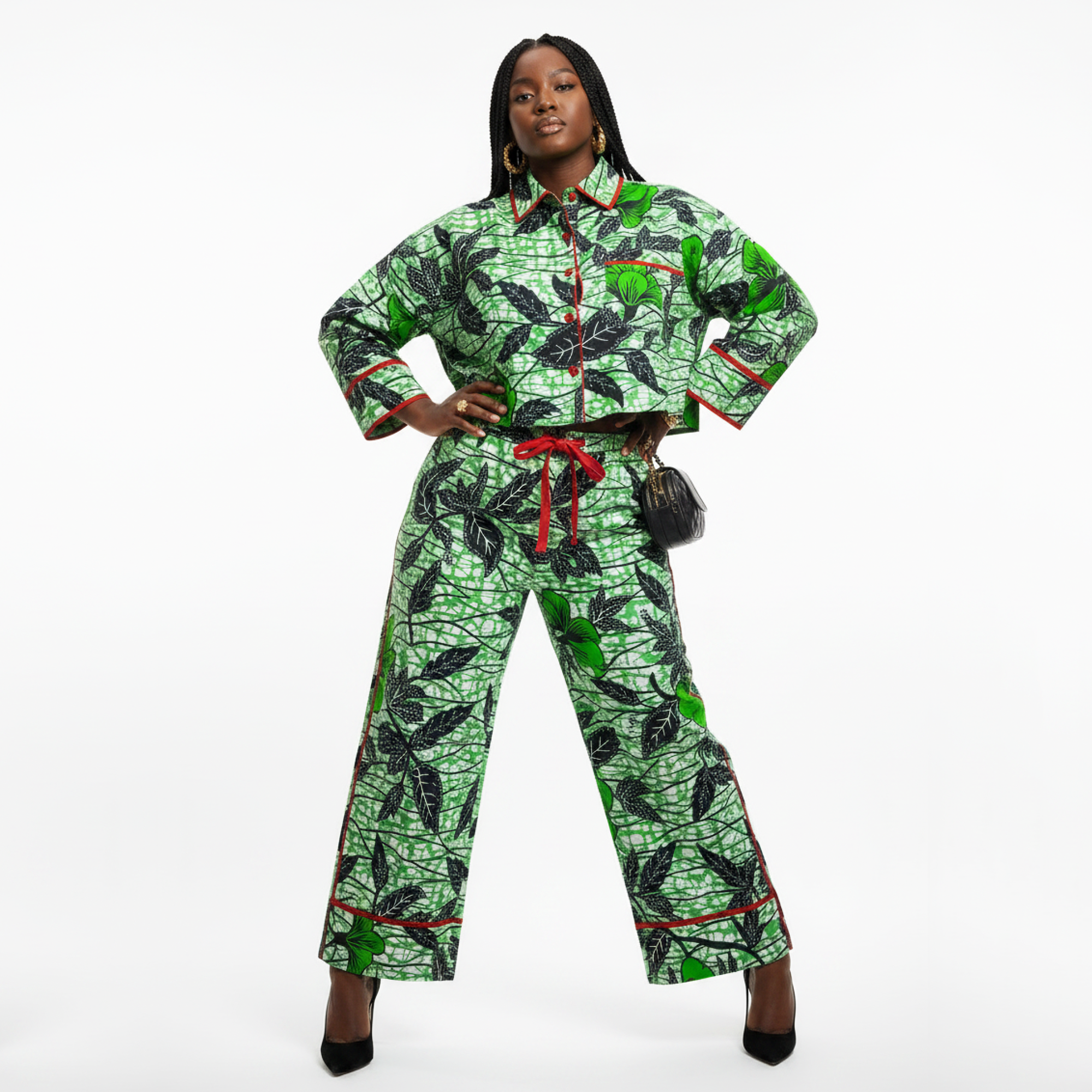 A woman modeling a matching two-piece pajama set with a green and black leaf pattern and red trim, standing against a plain white studio background.