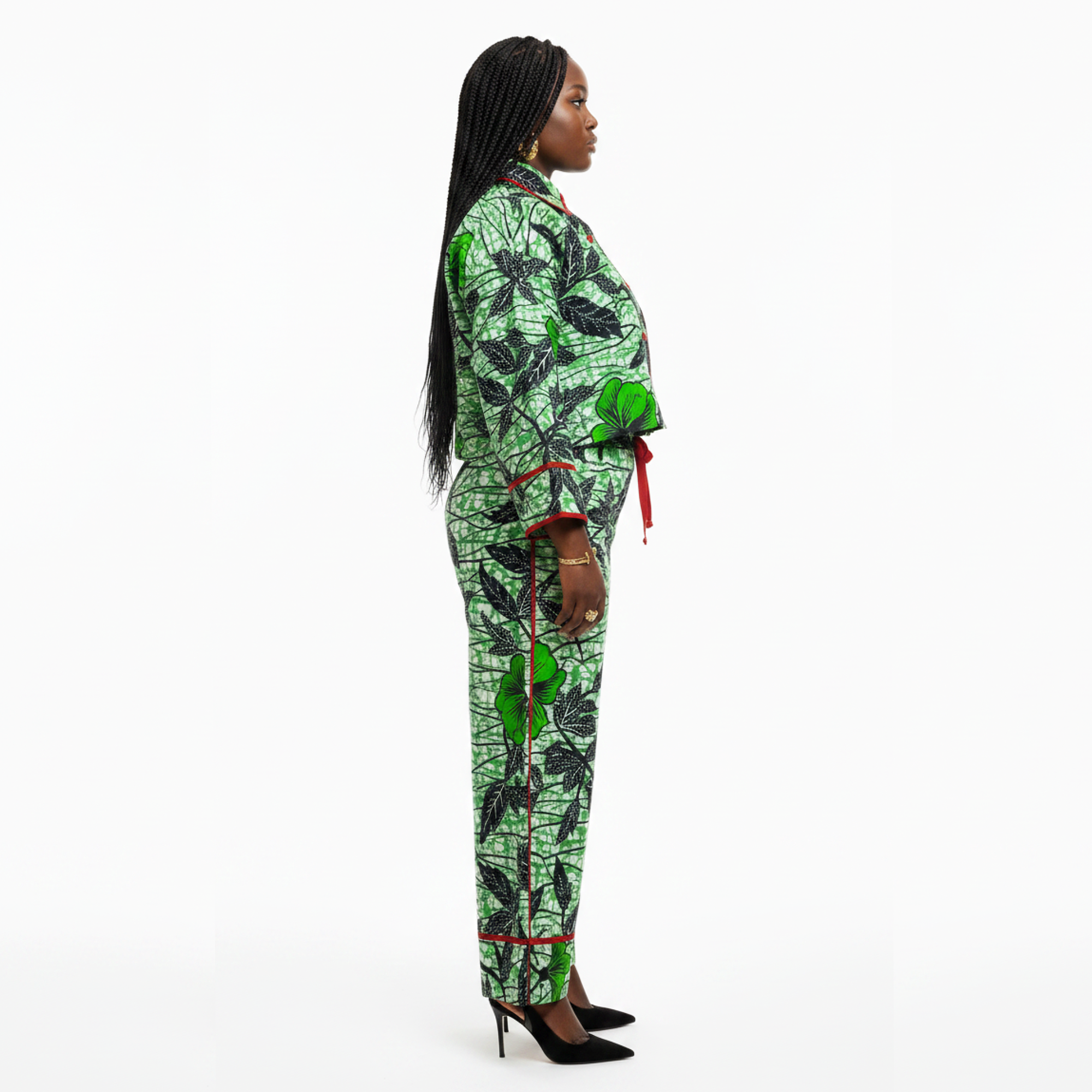 A woman shown in profile wearing a matching green and black patterned two-piece outfit with red trim details, standing against a plain white studio background.