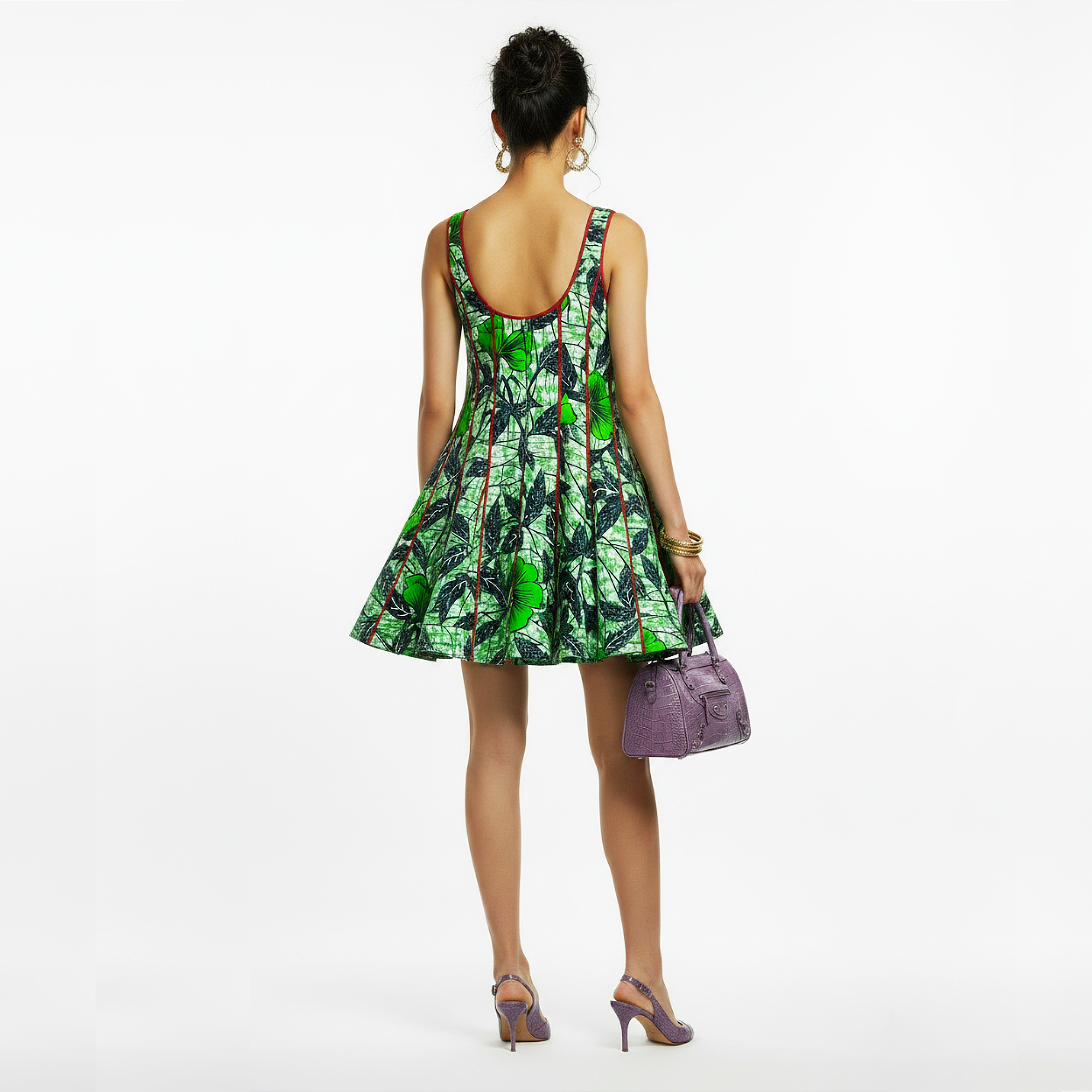 A woman shown from the back wearing a sleeveless green and black patterned dress with a flared skirt, holding a purple handbag and wearing purple heels against a plain white studio background.
