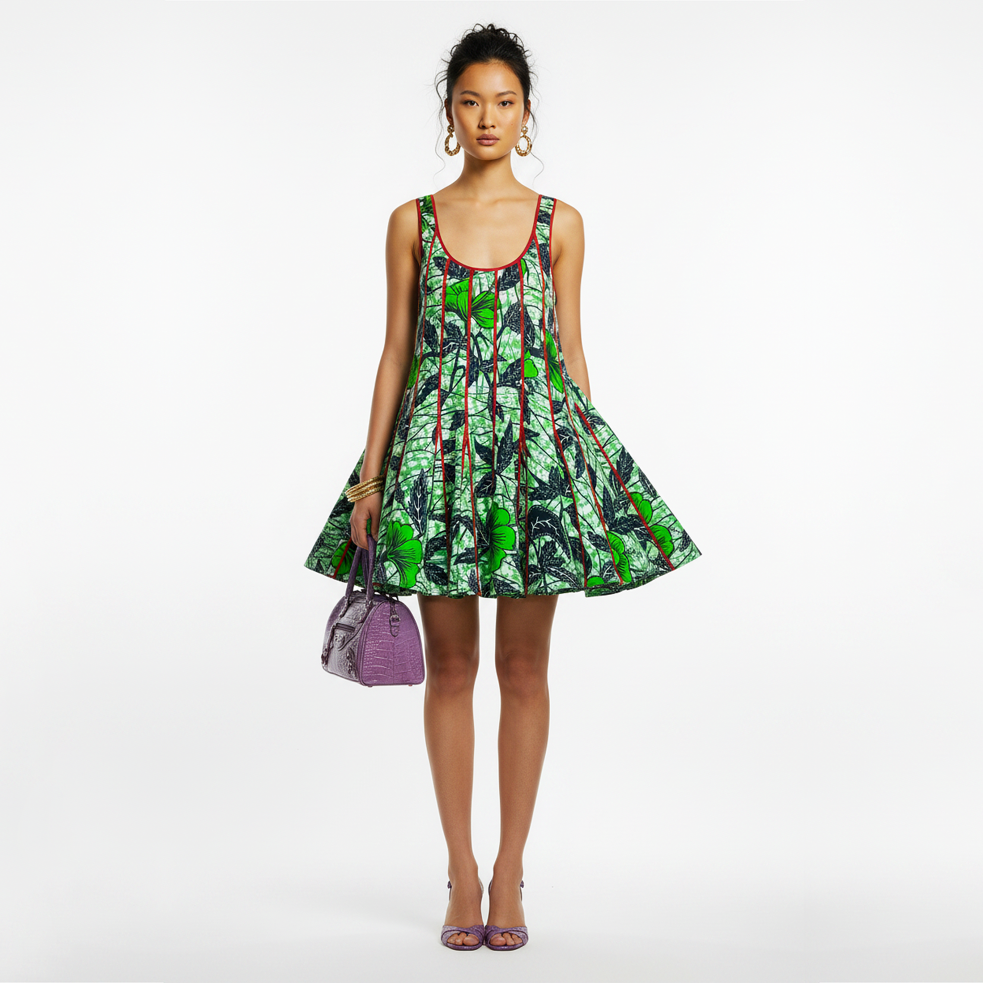 A model stands against a white studio background wearing a sleeveless fit-and-flare dress with a bold green, black, and red abstract print, holding a purple handbag.