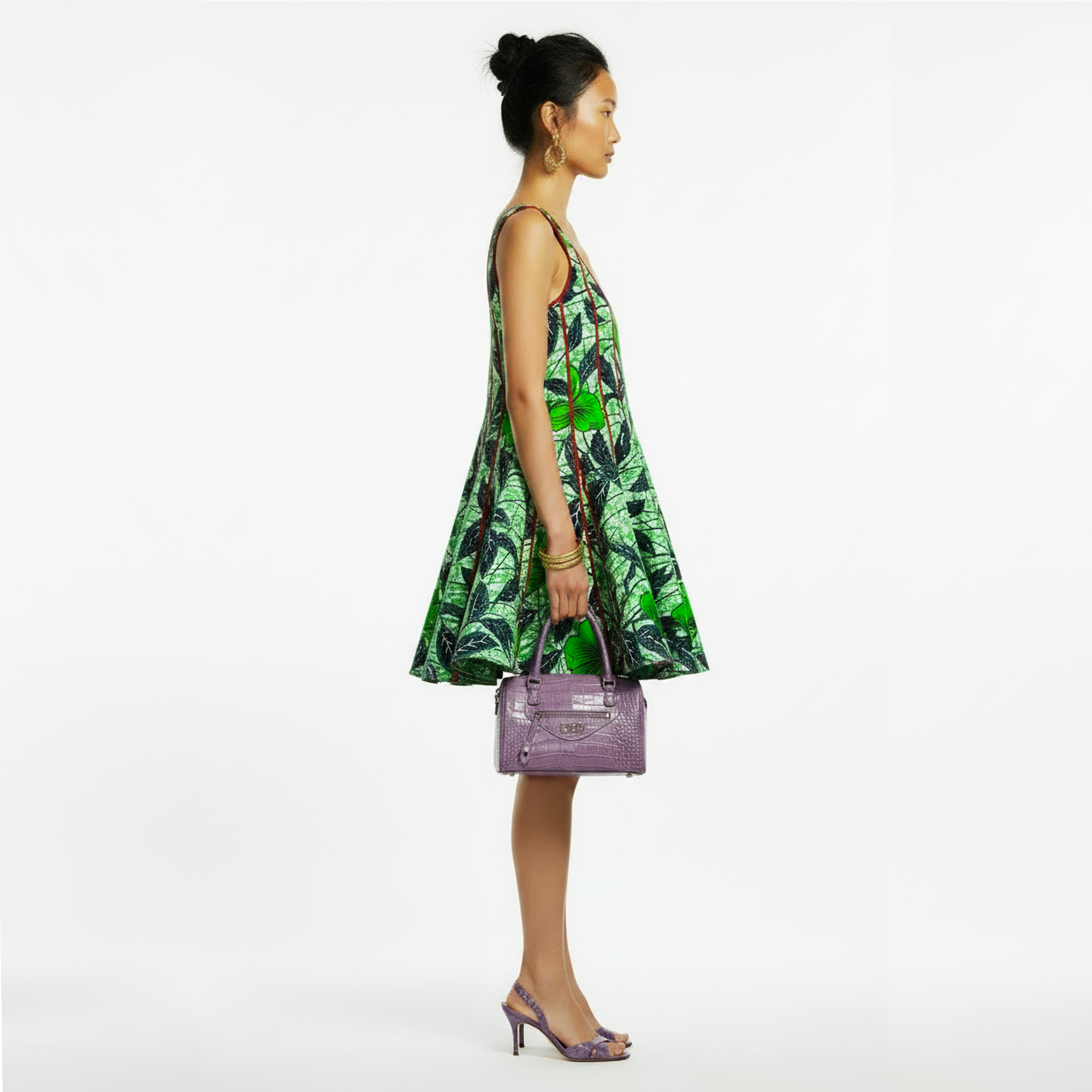 A model in profile wearing a sleeveless green tropical print dress and holding a purple handbag, set against a plain white studio background.
