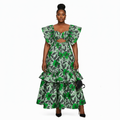A woman modeling a green and black tropical leaf print two-piece set consisting of a tiered maxi skirt and a matching ruffled crop top with a chest cutout, styled with black heels and a small black handbag against a plain white background.