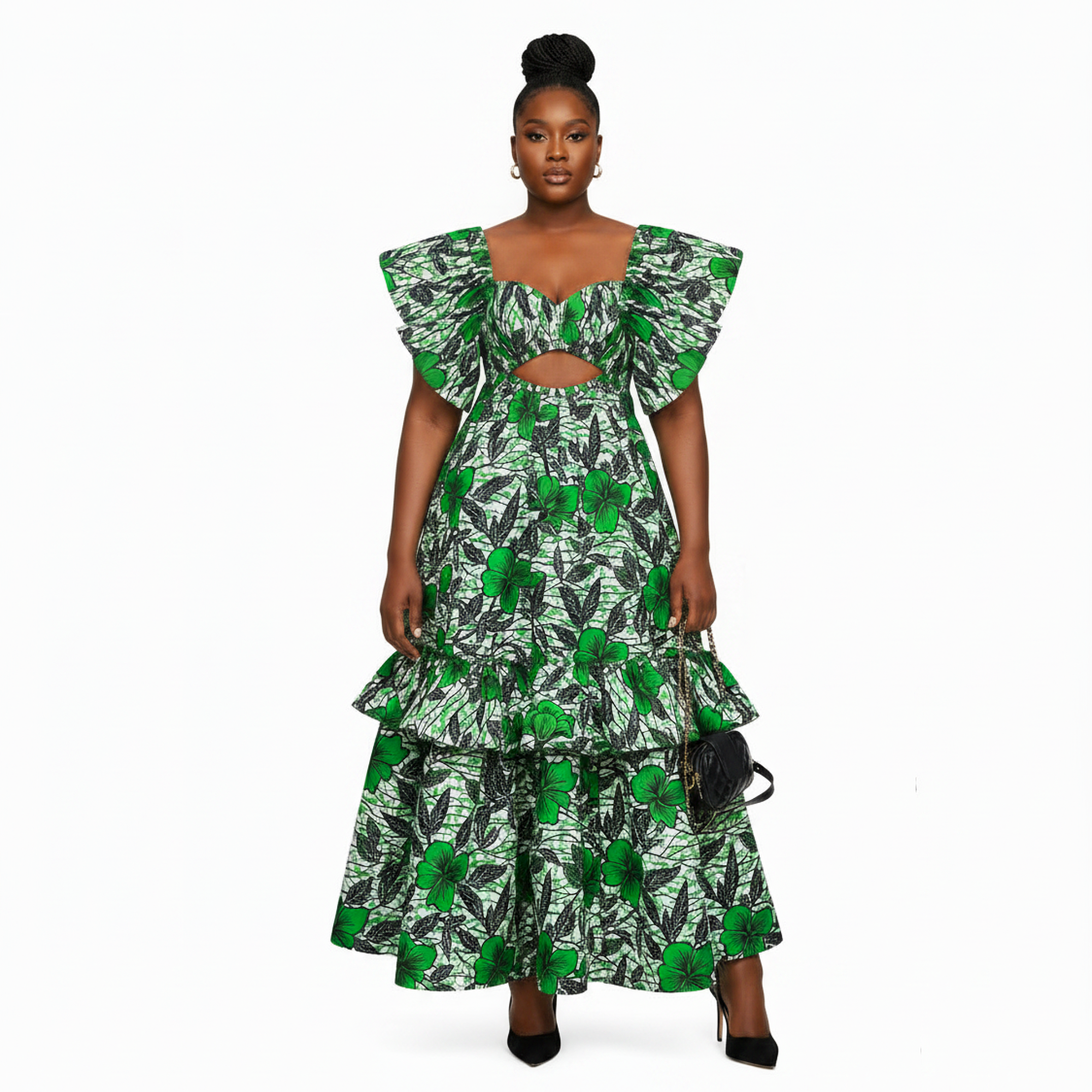 A woman modeling a green and black tropical leaf print two-piece set consisting of a tiered maxi skirt and a matching ruffled crop top with a chest cutout, styled with black heels and a small black handbag against a plain white background.
