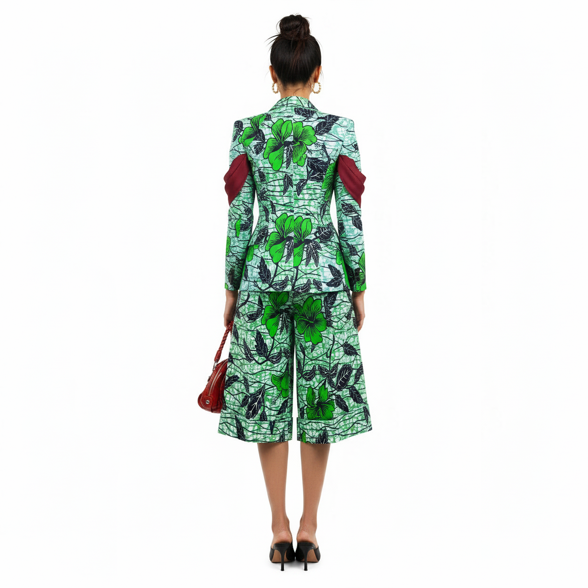 A woman shown from the back wearing a matching green and black floral print blazer and midi skirt set with red shoulder details, paired with a red handbag and black heels, against a plain white background.